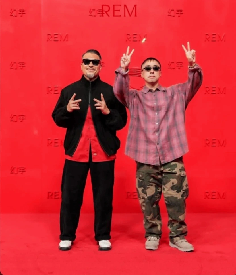 Two guests posing together in front of the red REM backdrop