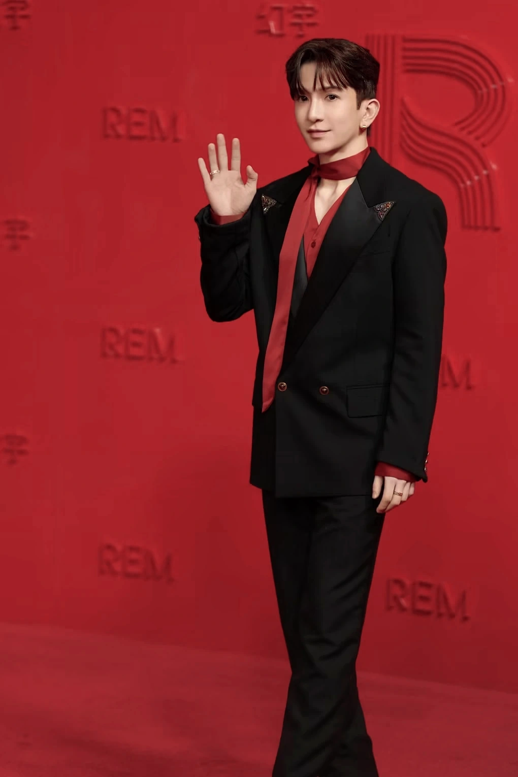 A guest in a black suit and red shirt on the REM red carpet