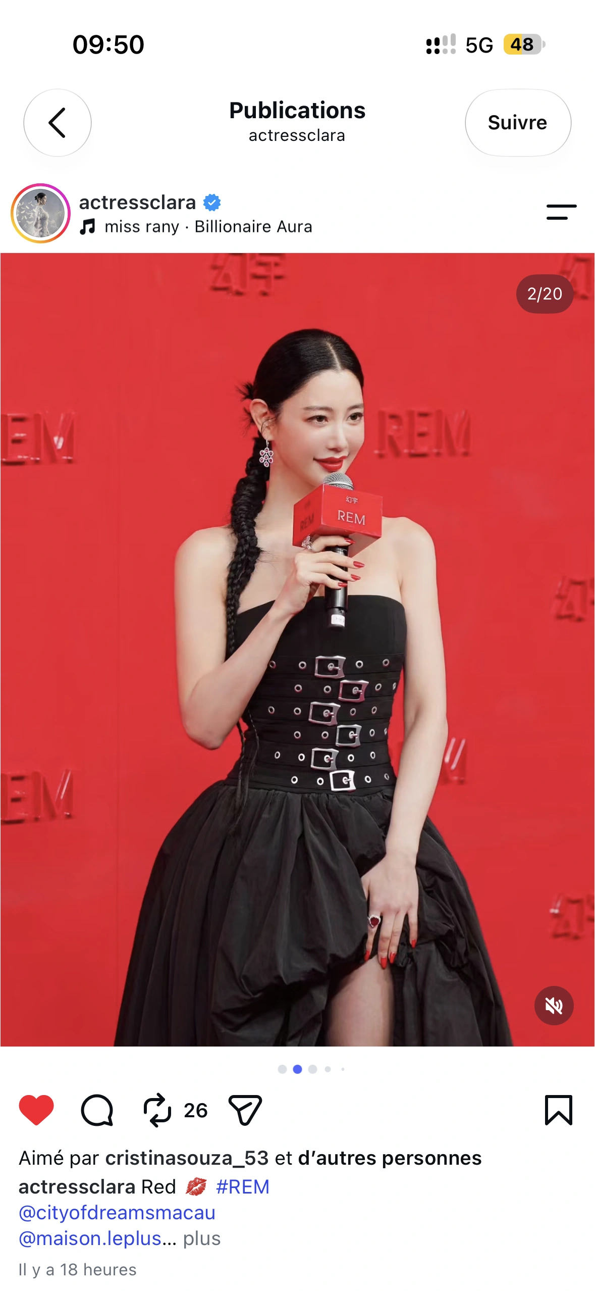 A smiling guest in a black dress holding a REM microphone on the red carpet